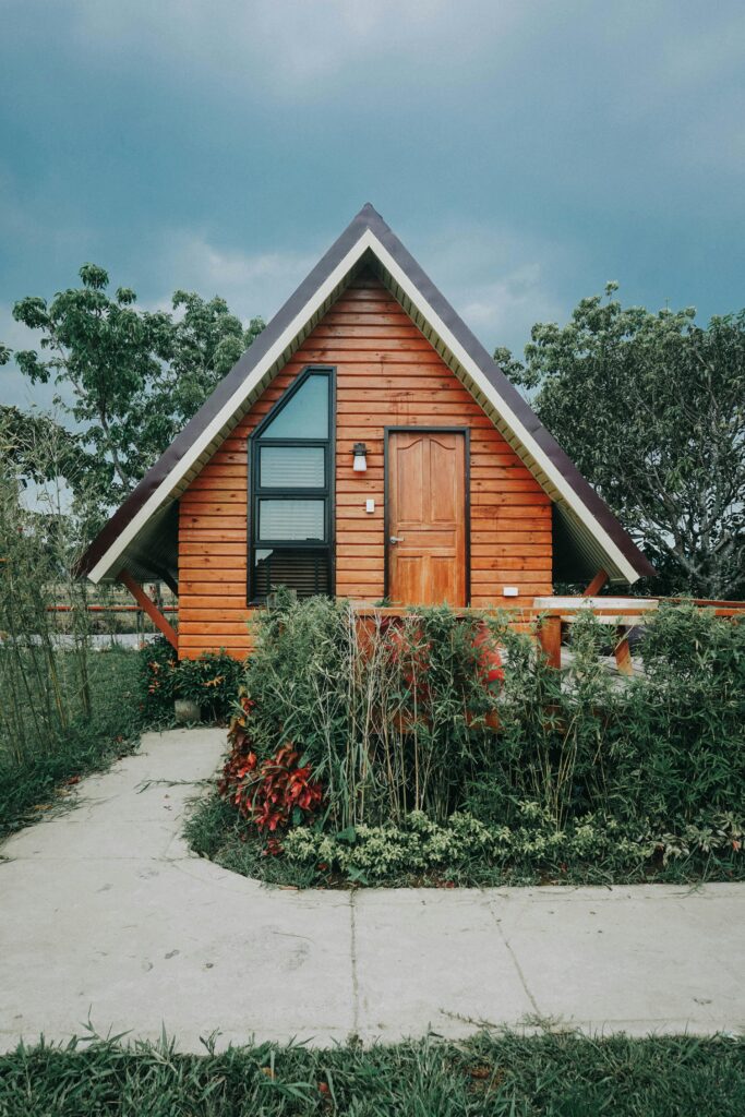 Charming wooden A-frame cabin surrounded by lush greenery and gardens, perfect for a peaceful retreat.